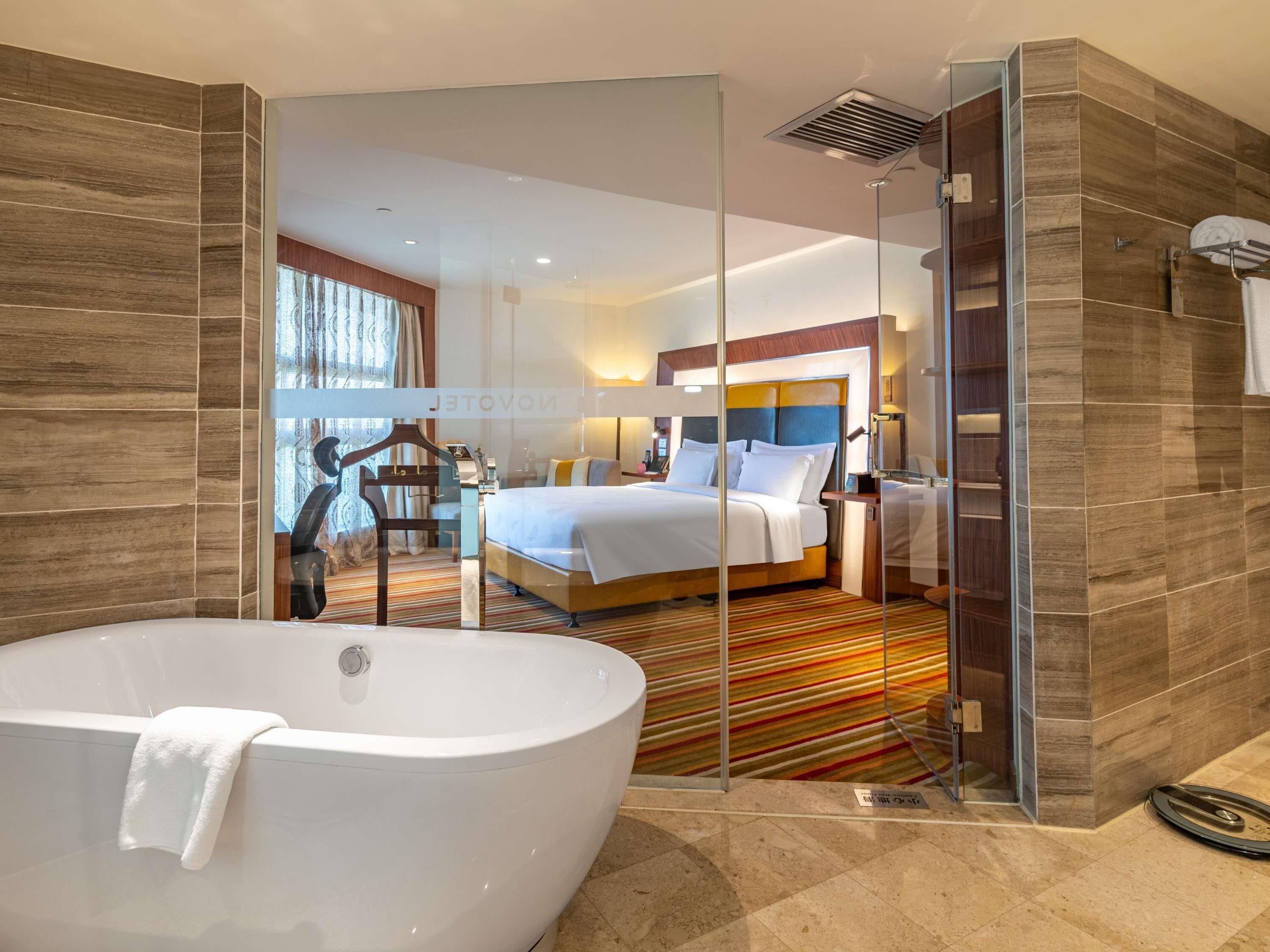 Ein modernes Hotelzimmer mit einer großen Badewanne, einem Bett mit weißen Leinen und einer gläsernen Duschkabine.