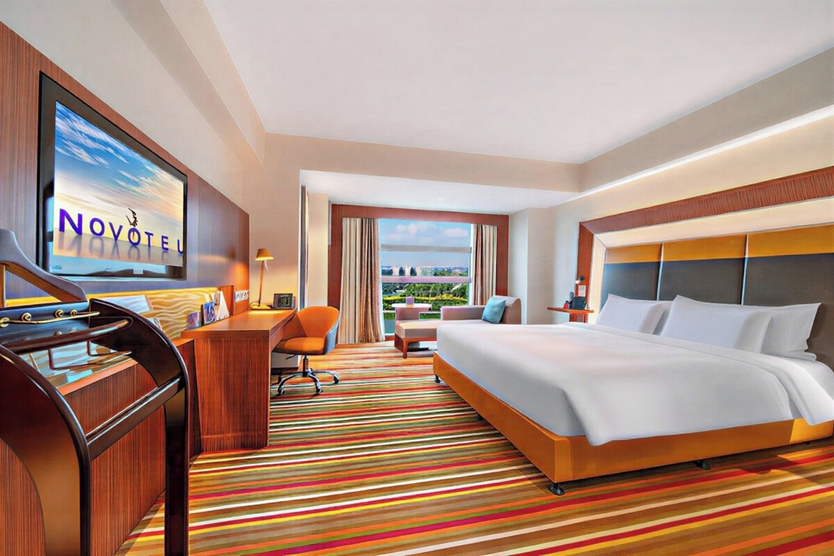 Habitación de hotel con cama, escritorio, silla, televisor y vista a la ciudad.