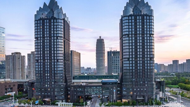 Dos edificios altos y modernos con un diseño arquitectónico distintivo, rodeados de otras estructuras elevadas en un entorno urbano.