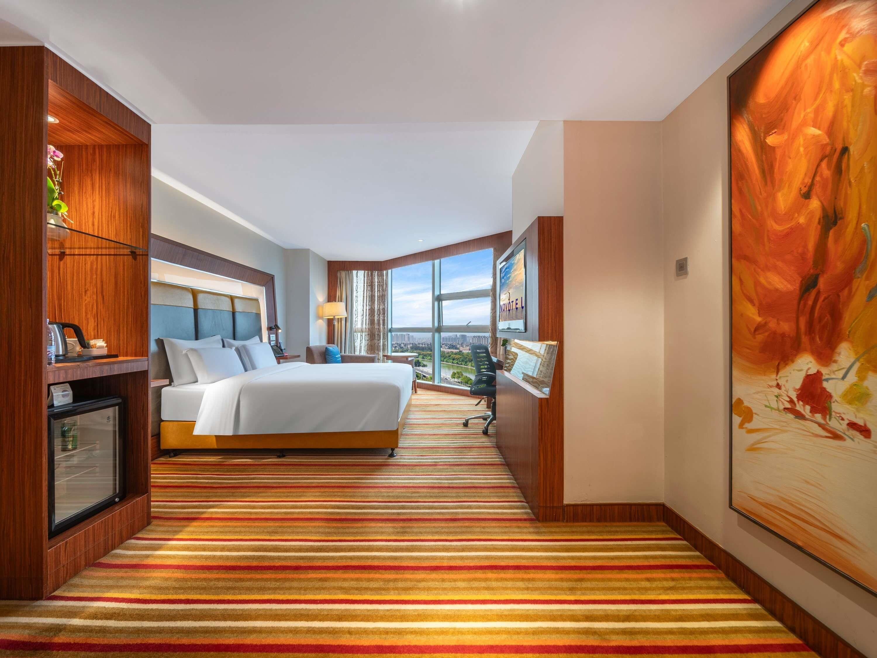 Habitación de hotel con una cama grande, un escritorio, una silla, un televisor y vistas a la ciudad.