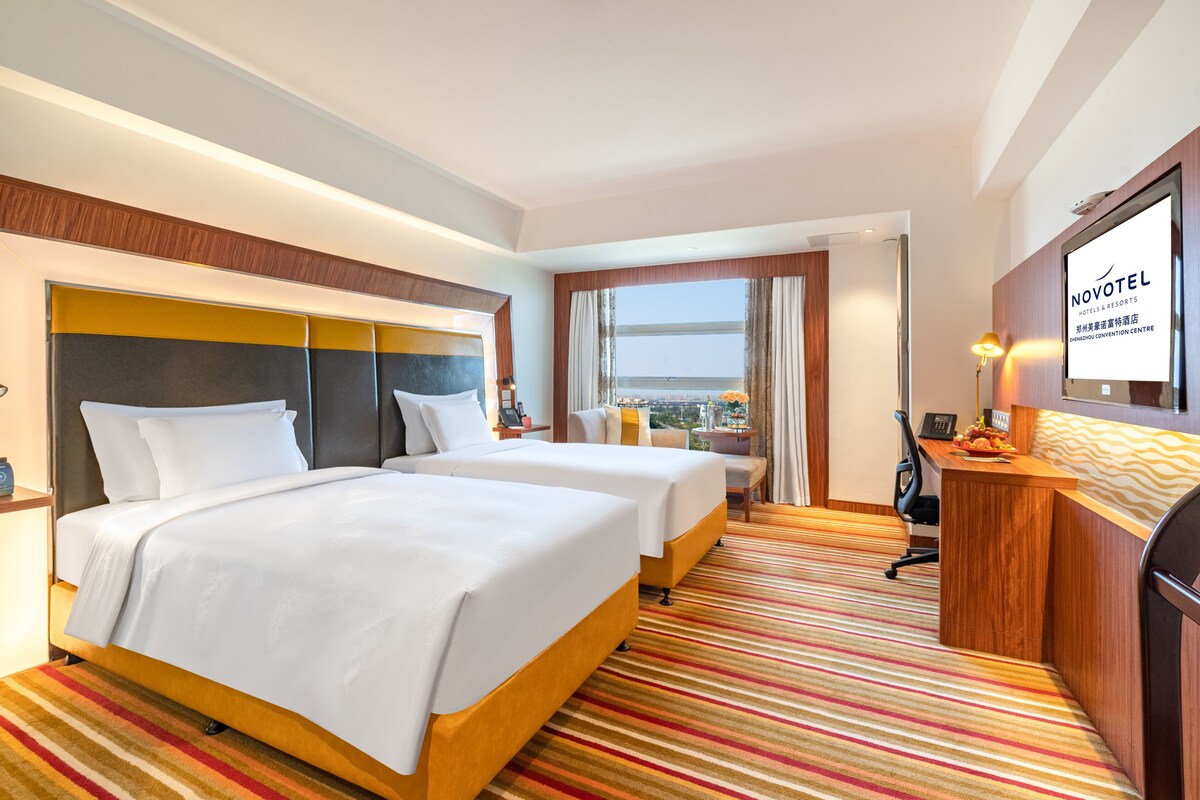 Una habitación de hotel con dos camas, un escritorio, un televisor y vistas a la ciudad.