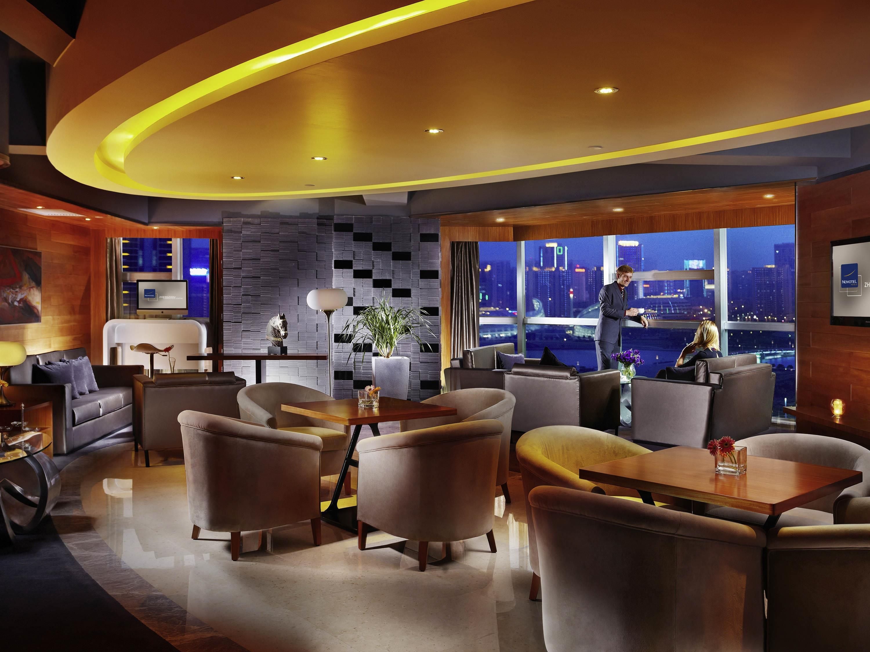 Un moderno vestíbulo de hotel con vistas a la ciudad, un televisor de pantalla plana y un área de estar con mesa y sillas.