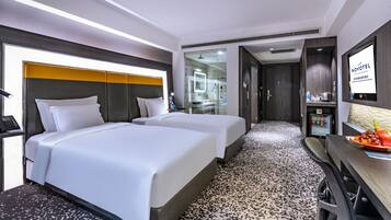 A hotel room with two beds, a desk with a chair, a shower area, and a TV mounted on the wall.