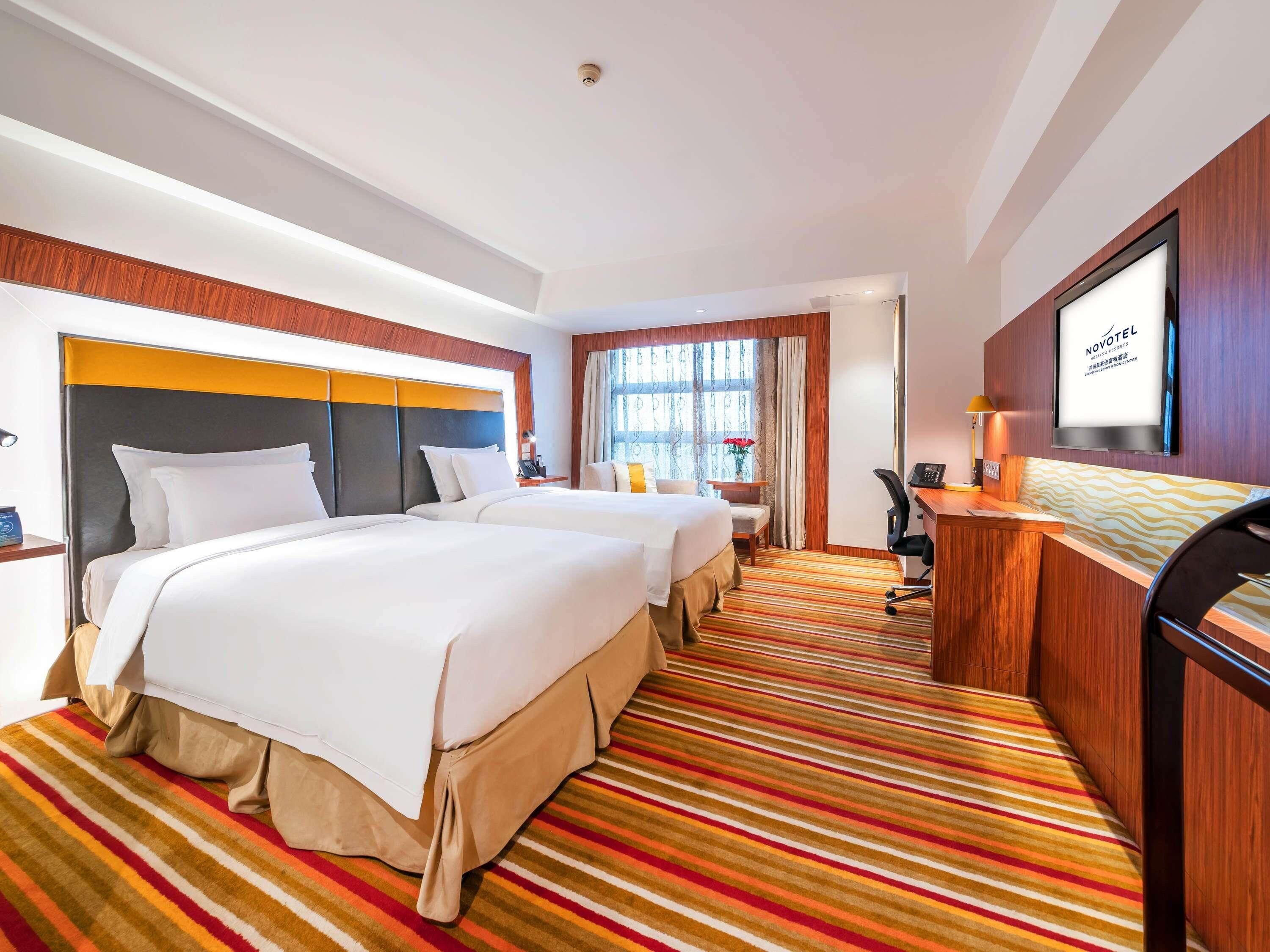 A hotel room with two beds, a desk, a chair, a TV, and a window with curtains.