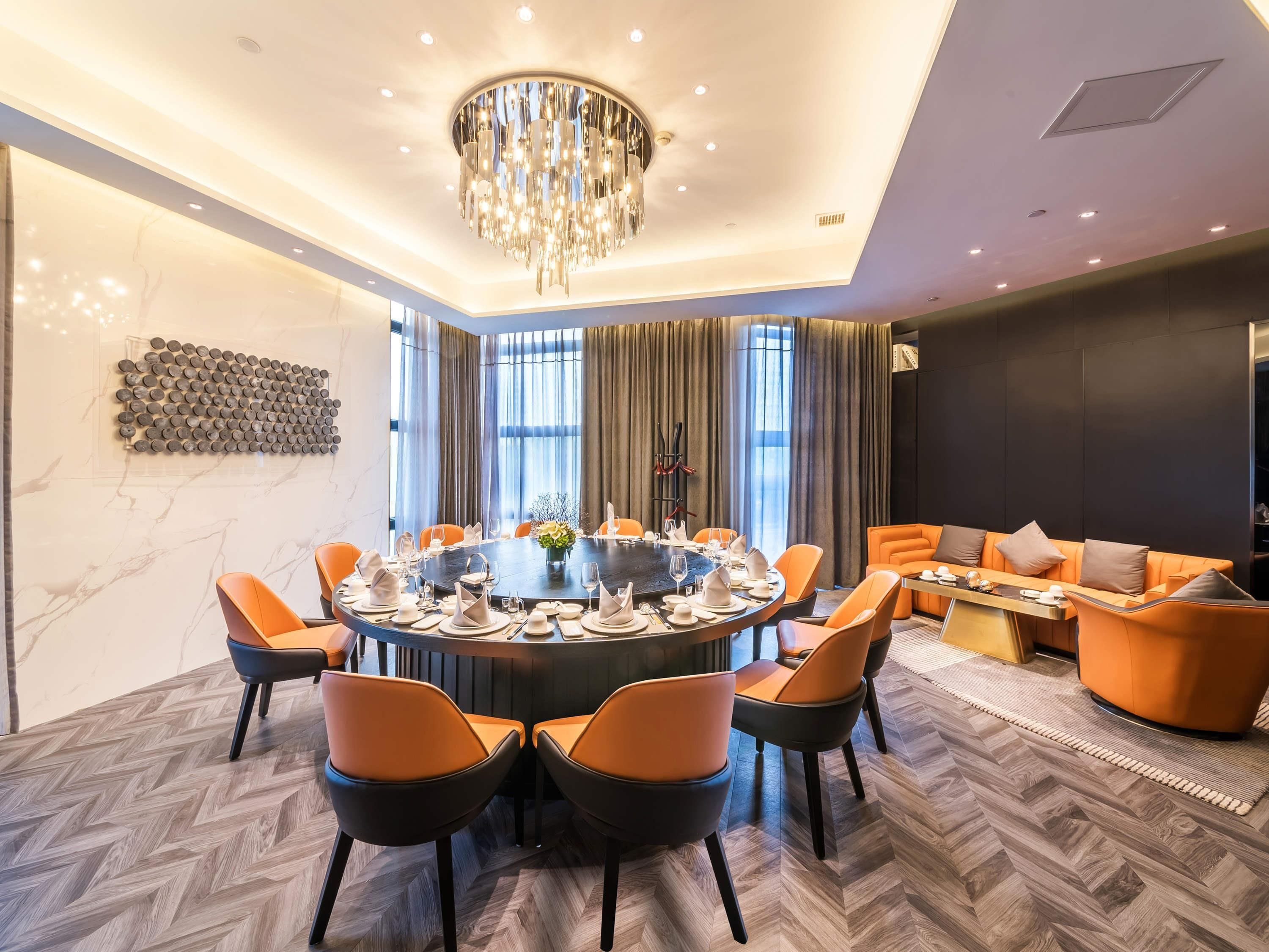 A modern dining area with a round table, orange chairs, and a chandelier.