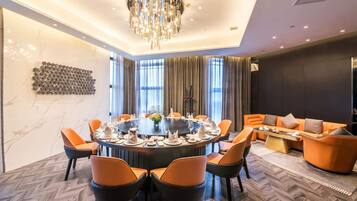 A modern dining area with a round table, orange chairs, and a chandelier.