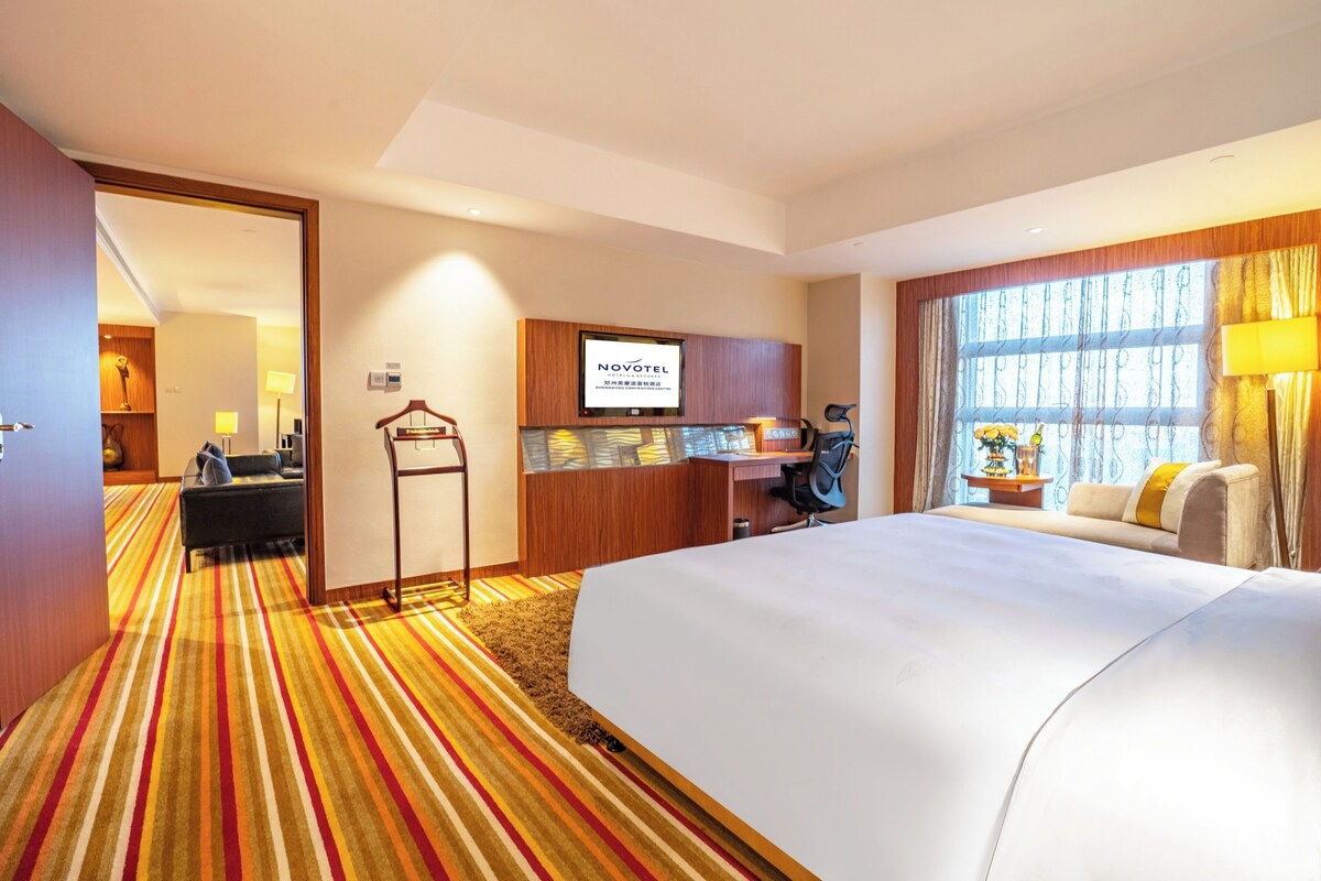 Habitación de hotel con una cama grande, un escritorio, una silla, un televisor y una ventana con cortinas.