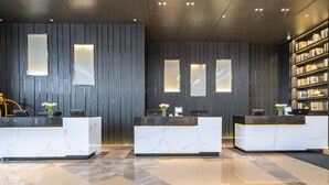 A reception area with marble counters, a dark wooden wall, and a bookshelf. - Novotel Zhengzhou Convention Centre (Zhengzhou)