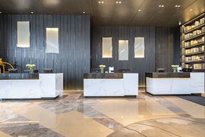 Un área de recepción con mostradores de mármol, pared de madera oscura y una estantería.