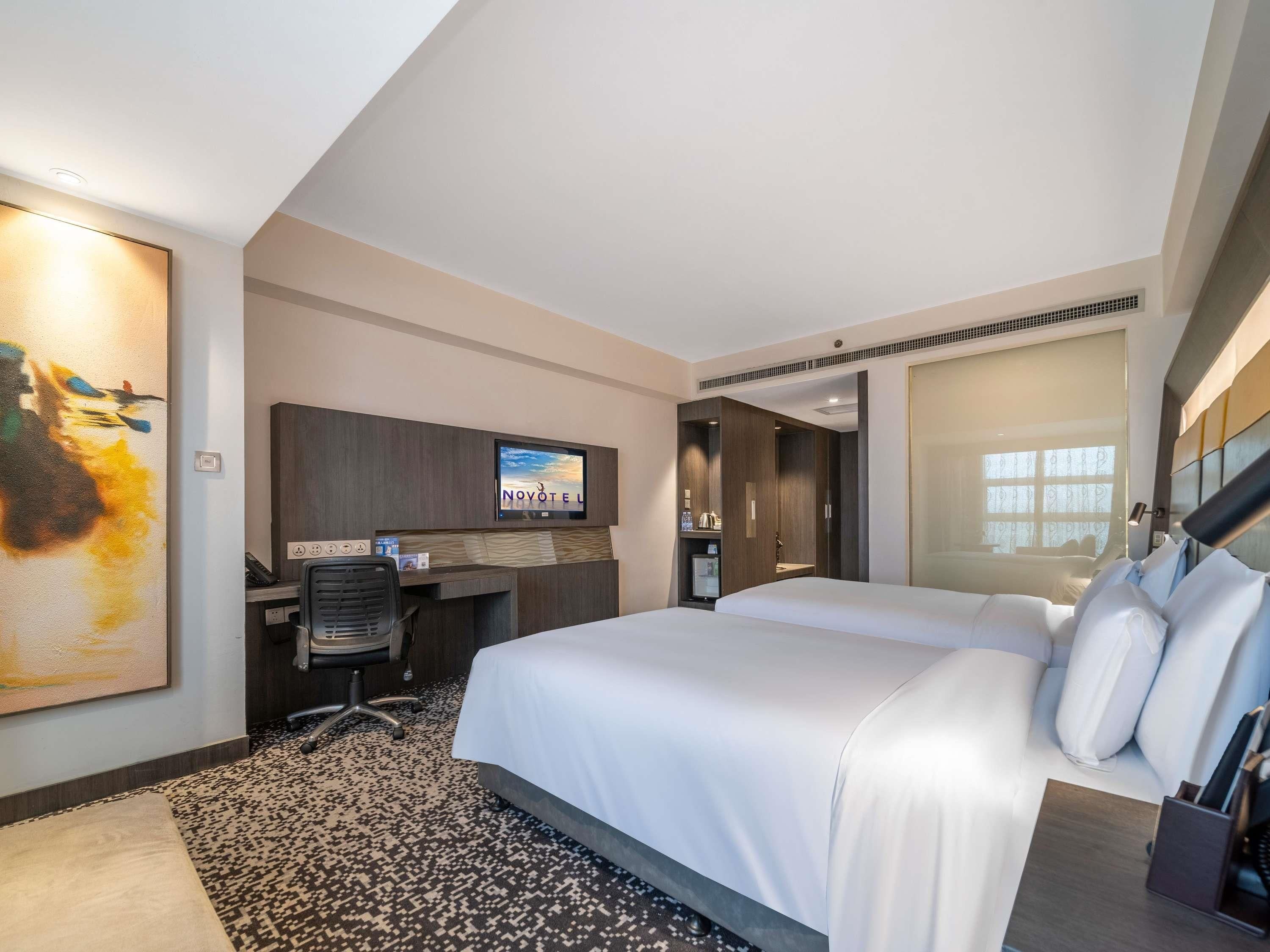 Quarto de hotel com cama, escrivaninha, televisão e um quadro na parede.