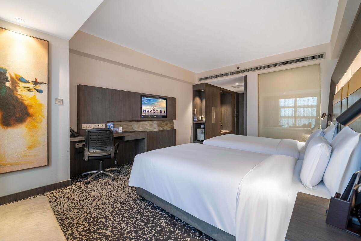 Una habitación de hotel con una cama, un escritorio, un televisor y un cuadro en la pared.
