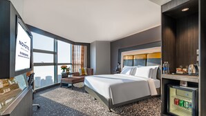Une chambre d’hôtel équipée d’un lit, d’un bureau, d’un mini-bar et d’une grande fenêtre.