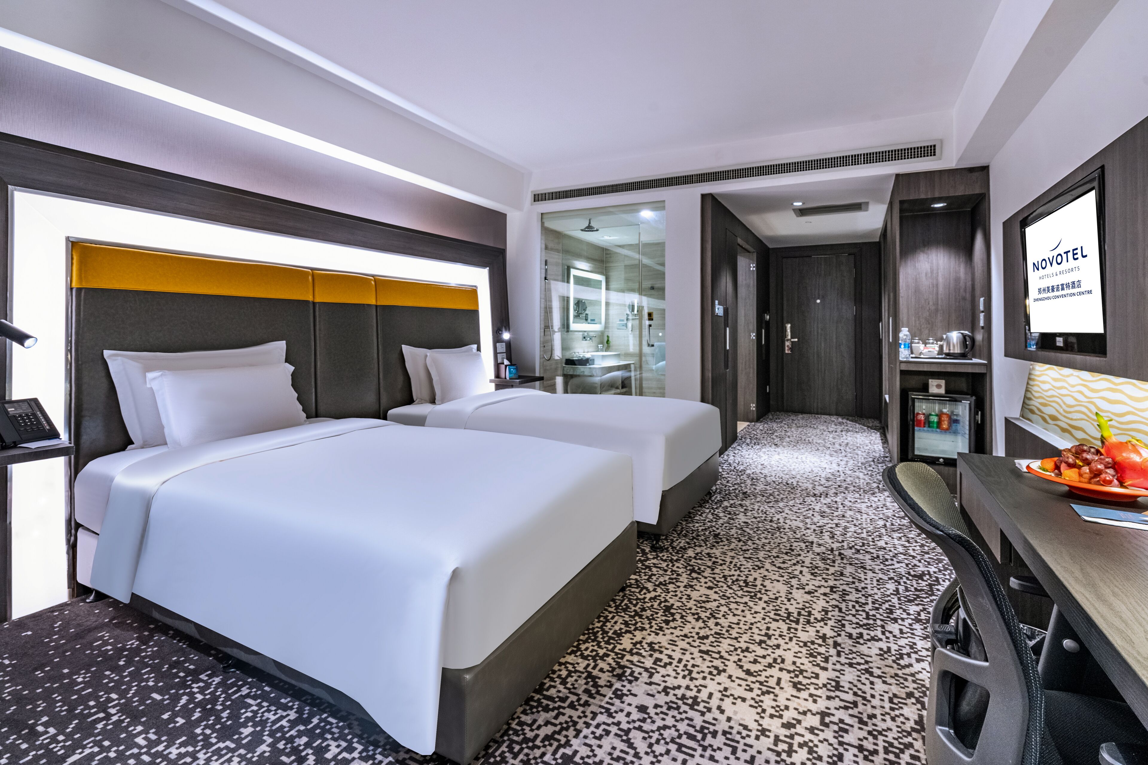 Een hotelkamer met twee bedden, een bureau met een computer, een televisie en een douche.