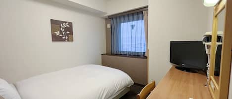 A hotel room with a single bed, a desk with a telephone, a television, and a window with curtains.