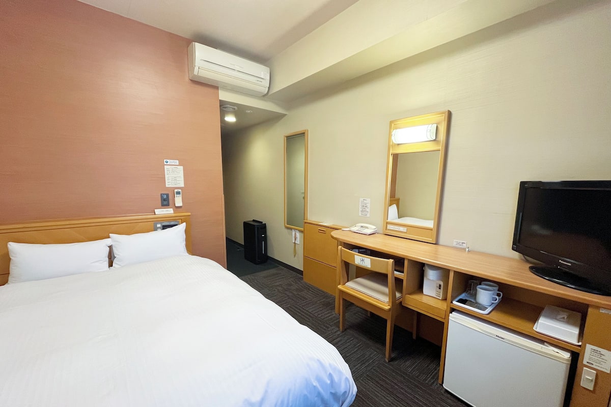A hotel room with a bed, a desk with a computer, a television, and a small refrigerator.