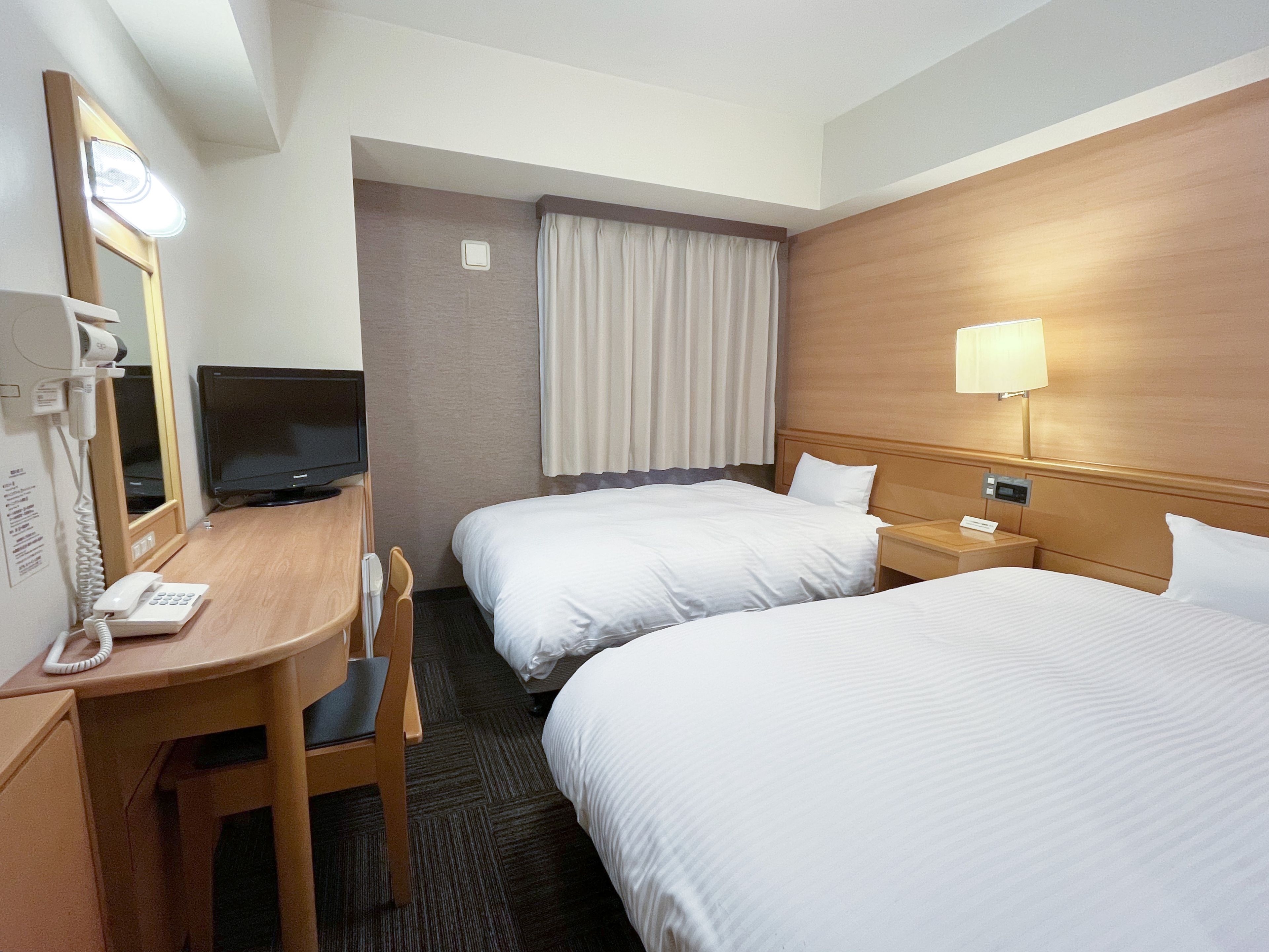A hotel room with two beds, a desk with a telephone, a television, and a mirror.