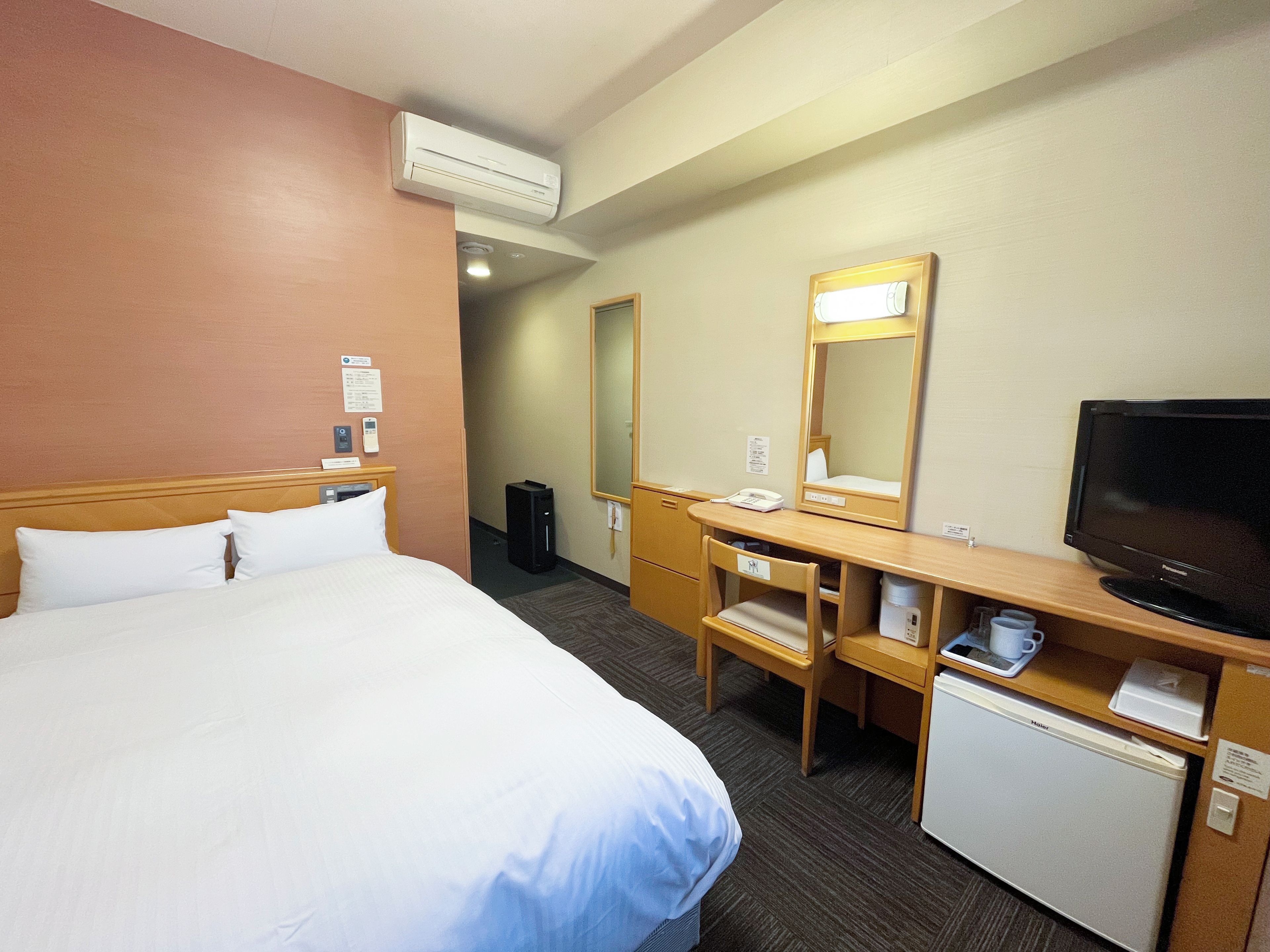 Una habitación de hotel con cama, escritorio con computadora, televisor y un refrigerador pequeño.