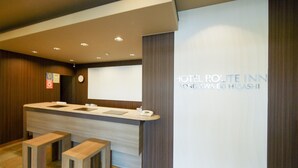 A reception desk with a counter, two wooden stools, a clock, and a wall with the text "HOTEL ROUTE INN YONEZAWA EX HIGASHI". - Hotel Route-Inn Yonezawa Ekihigashi (Yonezawa)