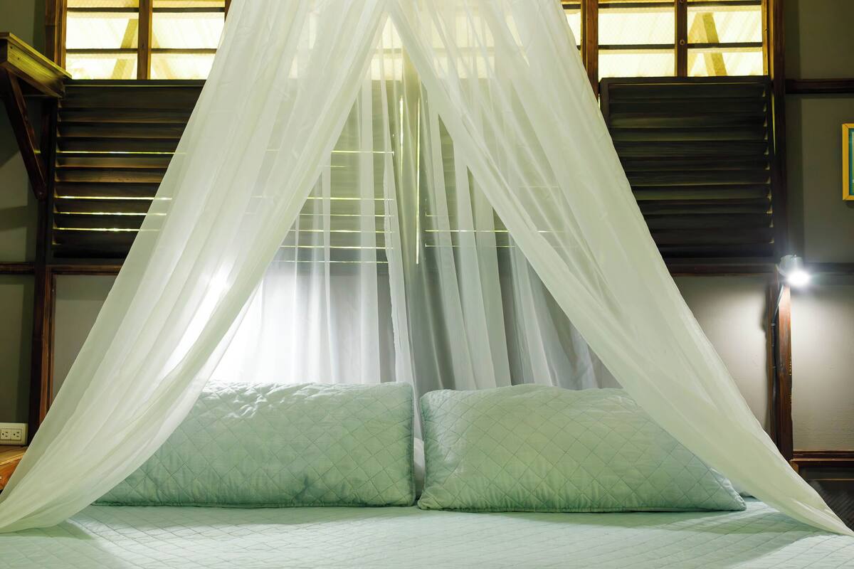 A bed with a canopy, a window with blinds, and a wall-mounted light.