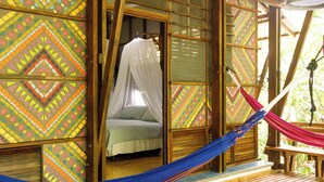 A room with a bed under a canopy, a hammock, and patterned walls. - La Kukula Lodge (Cahuita)
