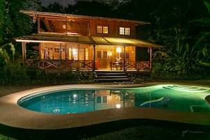 Uma casa de madeira de dois andares com uma piscina em frente.