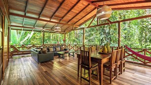 A wooden deck with a dining table, chairs, and a sofa. - La Kukula Lodge (Cahuita)