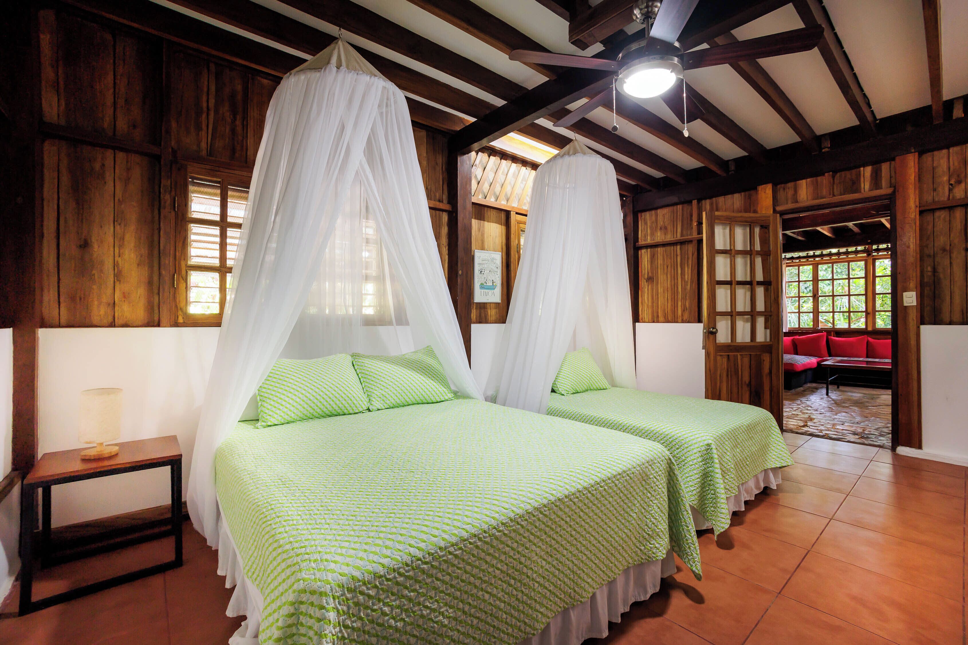 Una habitación con dos camas, paredes de madera, una mesita y un sofá rojo.