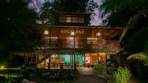 A two-story wooden building with a thatched roof, surrounded by lush greenery. - La Kukula Lodge (Cahuita)