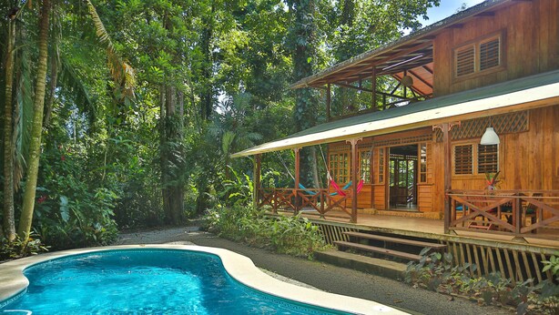 A wooden house with a pool surrounded by lush greenery. - La Kukula Lodge (Cahuita)