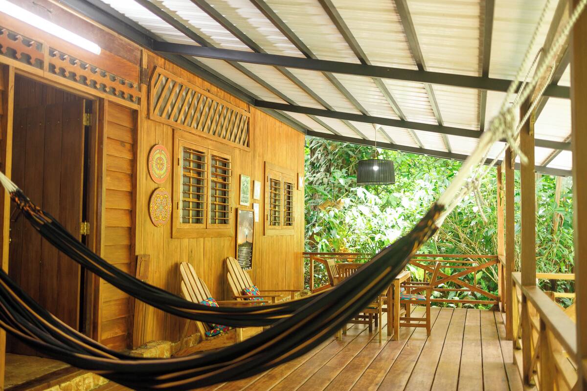 A wooden deck with a hammock, wooden chairs, and a table.