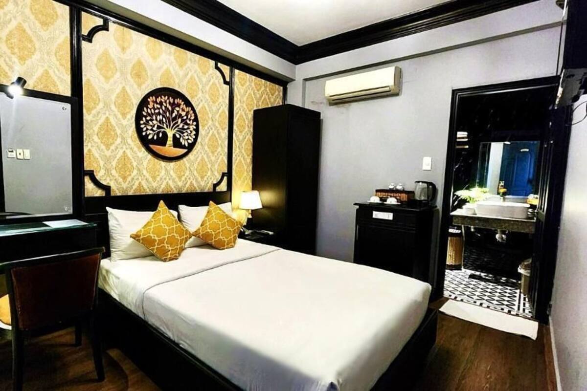 A hotel room with a bed, a desk with a chair, a mirror, a wardrobe, and a bathroom visible through an open door.