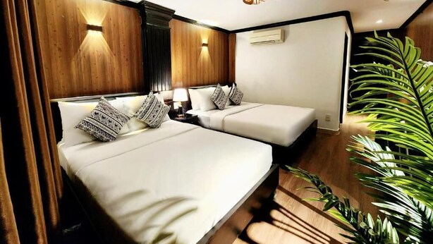 Ein Hotelzimmer mit zwei Betten, einem Deckenventilator und einer großen Pflanze.