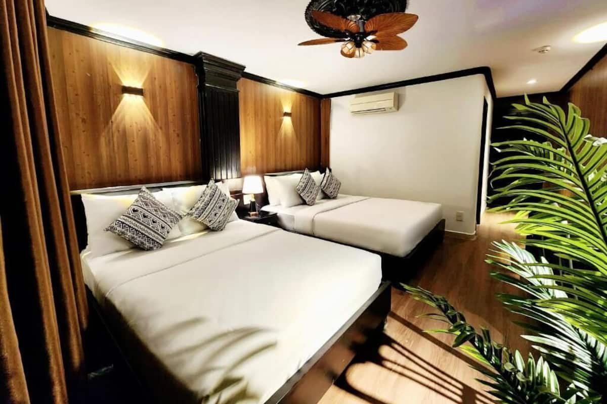 A hotel room with two beds, a ceiling fan, and a large plant.