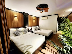 Habitación de hotel con dos camas, un ventilador de techo y una planta grande.