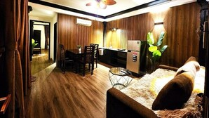 Ein modernes Wohnzimmer mit Sofa, Essbereich mit Stühlen, Küche mit Kühlschrank und Deckenventilator.