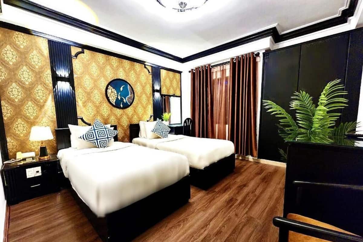 A hotel room with two beds, a large mirror, a chandelier, and a potted plant.