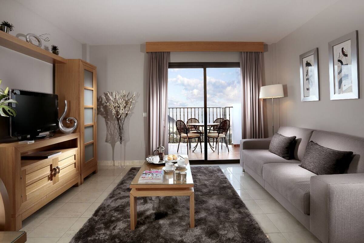 A modern living room with a sofa, a coffee table, a TV, and a dining area with chairs and a table.