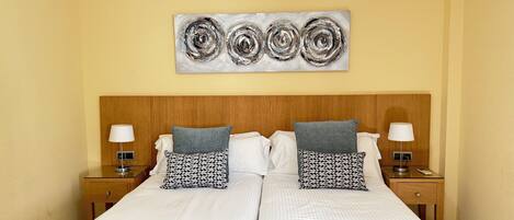 Un lit double avec une tête de lit en bois, deux tables de chevet avec des lampes et une œuvre d’art abstraite accrochée au mur.
