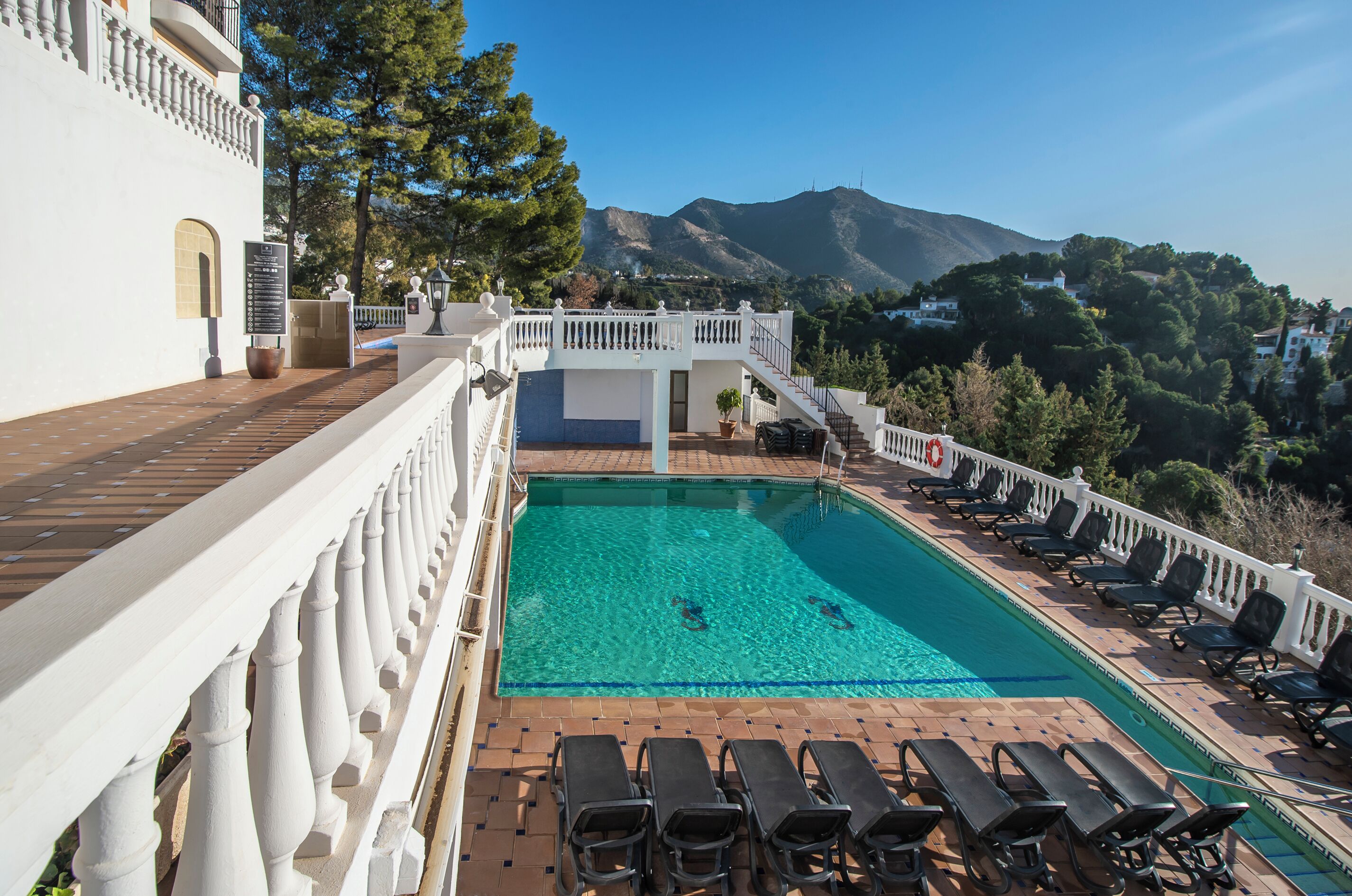 Una piscina con vistas a las montañas, un balc ón blanco con sillas y un cartel.