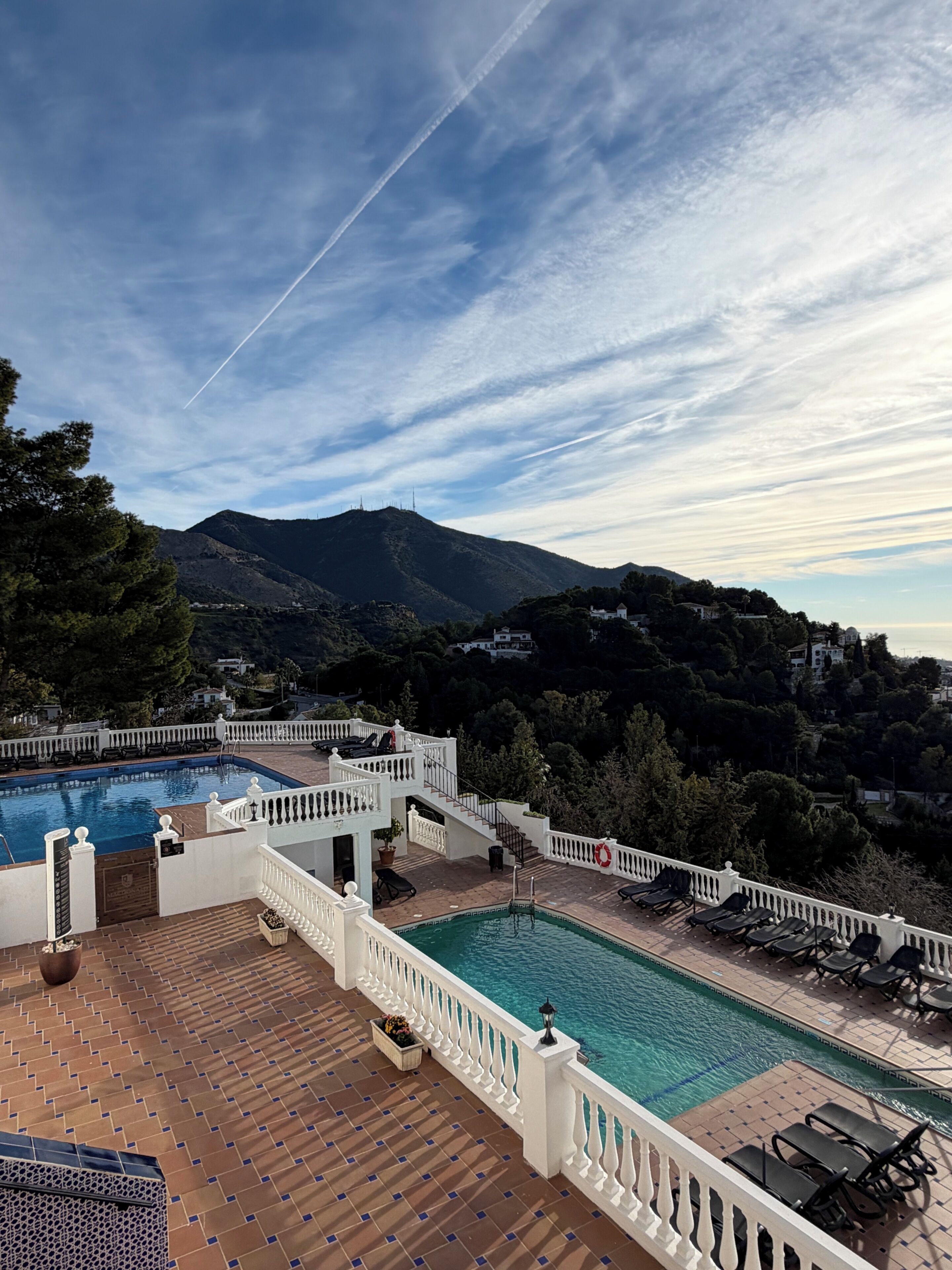 A rooftop pool with a view of a mountain, white railings, and lounge chairs.