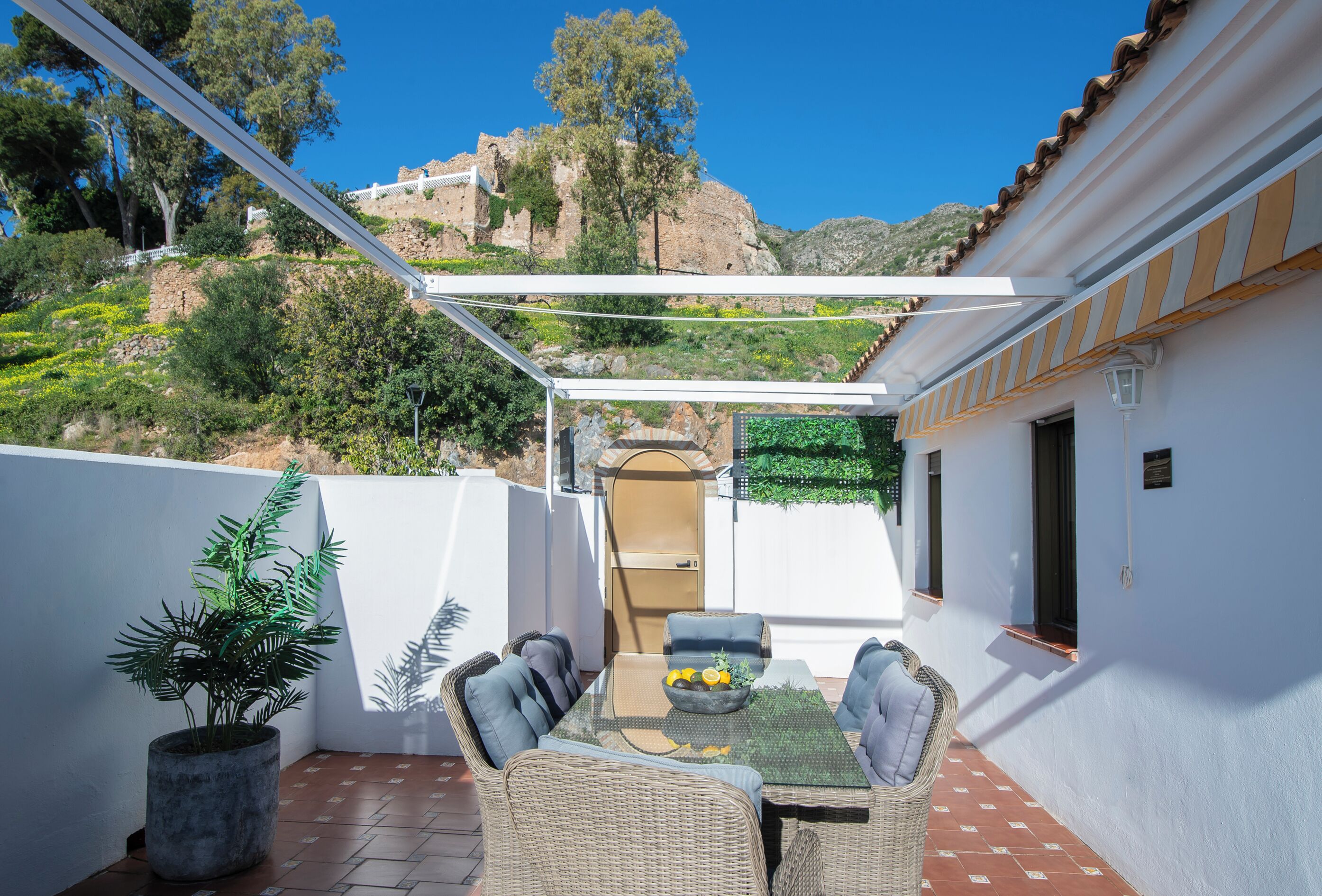 Un patio con mobiliario de mimbre, una mesa de vidrio y una planta en maceta.