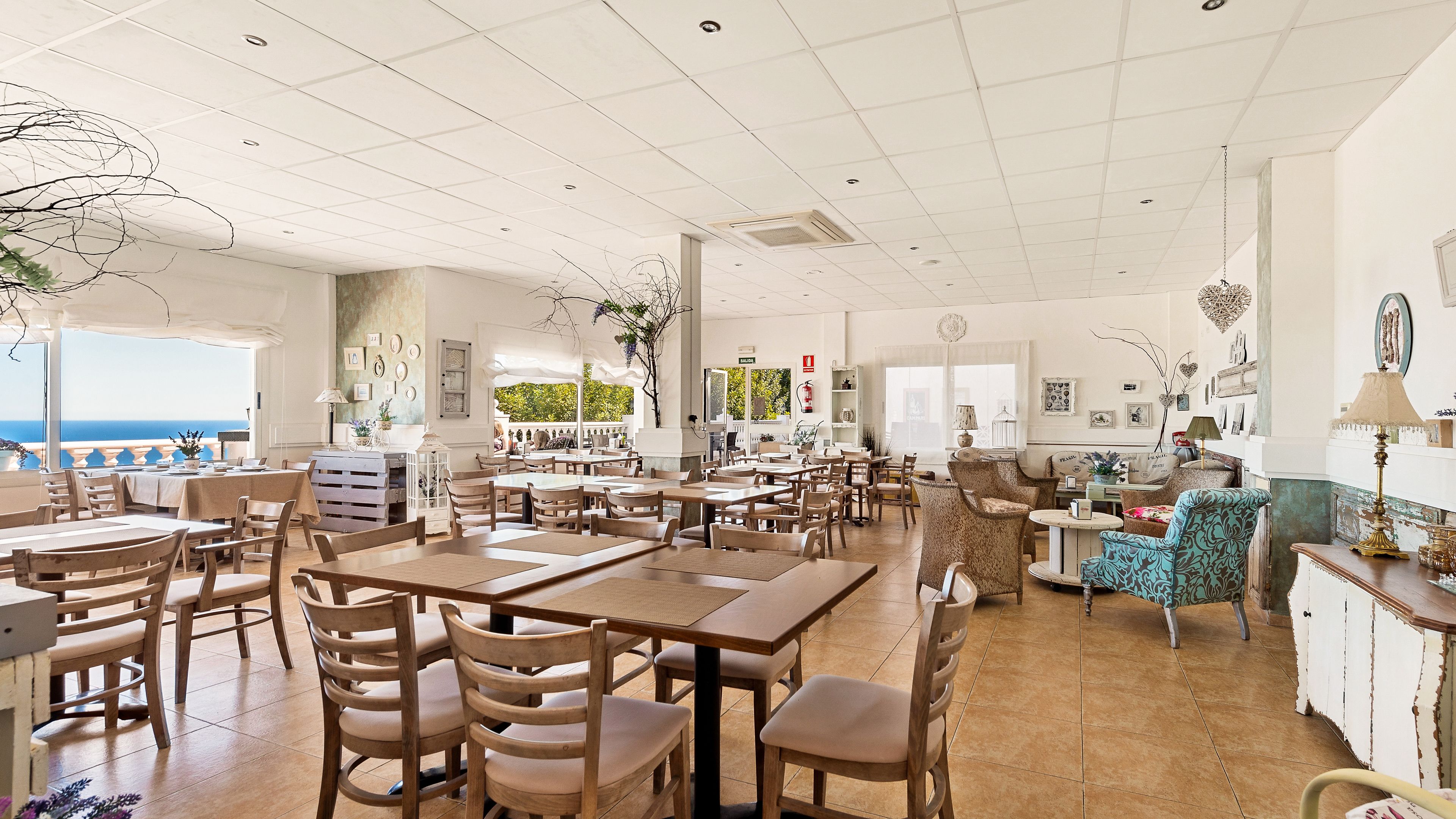 A spacious dining area with multiple tables and chairs, a view of the sea, and a balcony.