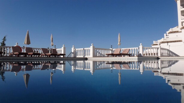 A poolside area with lounge chairs and umbrellas, reflecting in the water. - Macdonald La Ermita Resort (Mijas)