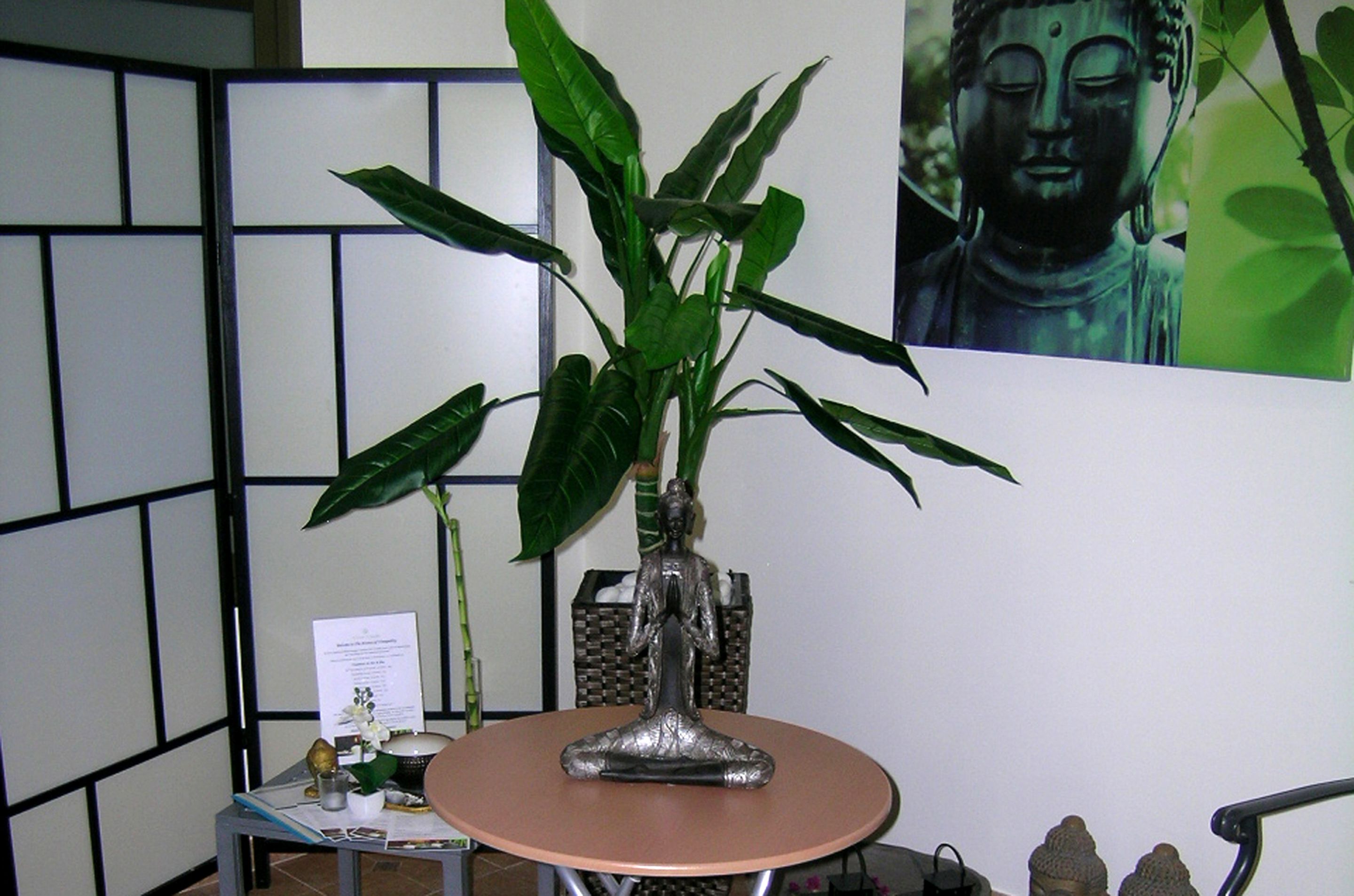Una habitación con una mesa redonda, una planta en maceta, una estatua de Buda y una pequeña estatua sobre la mesa.