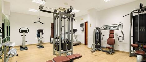 A gym with various exercise machines, a bench press, and a mirrored wall.