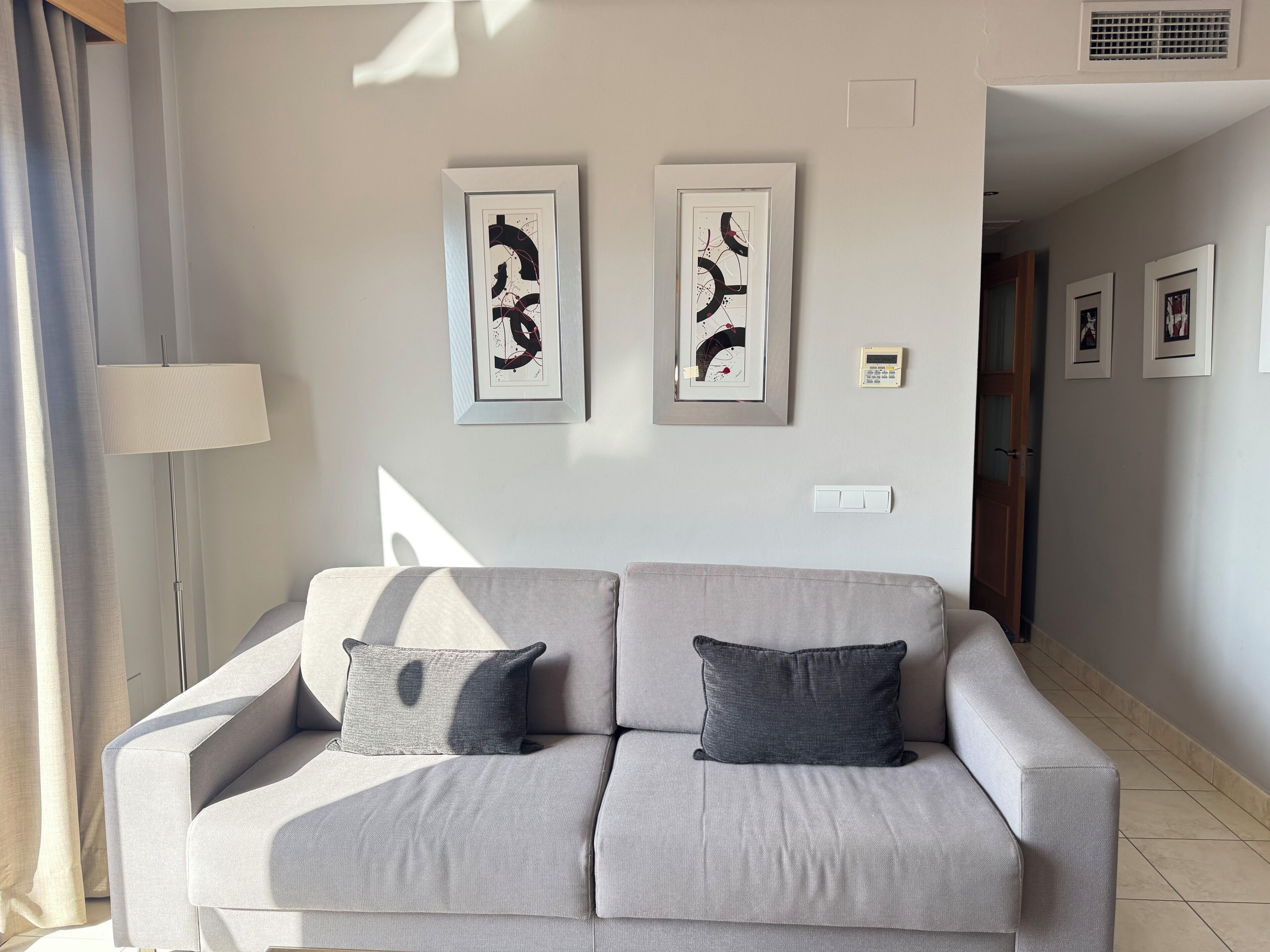 A modern living room with a grey sofa, two cushions, and abstract art on the wall.