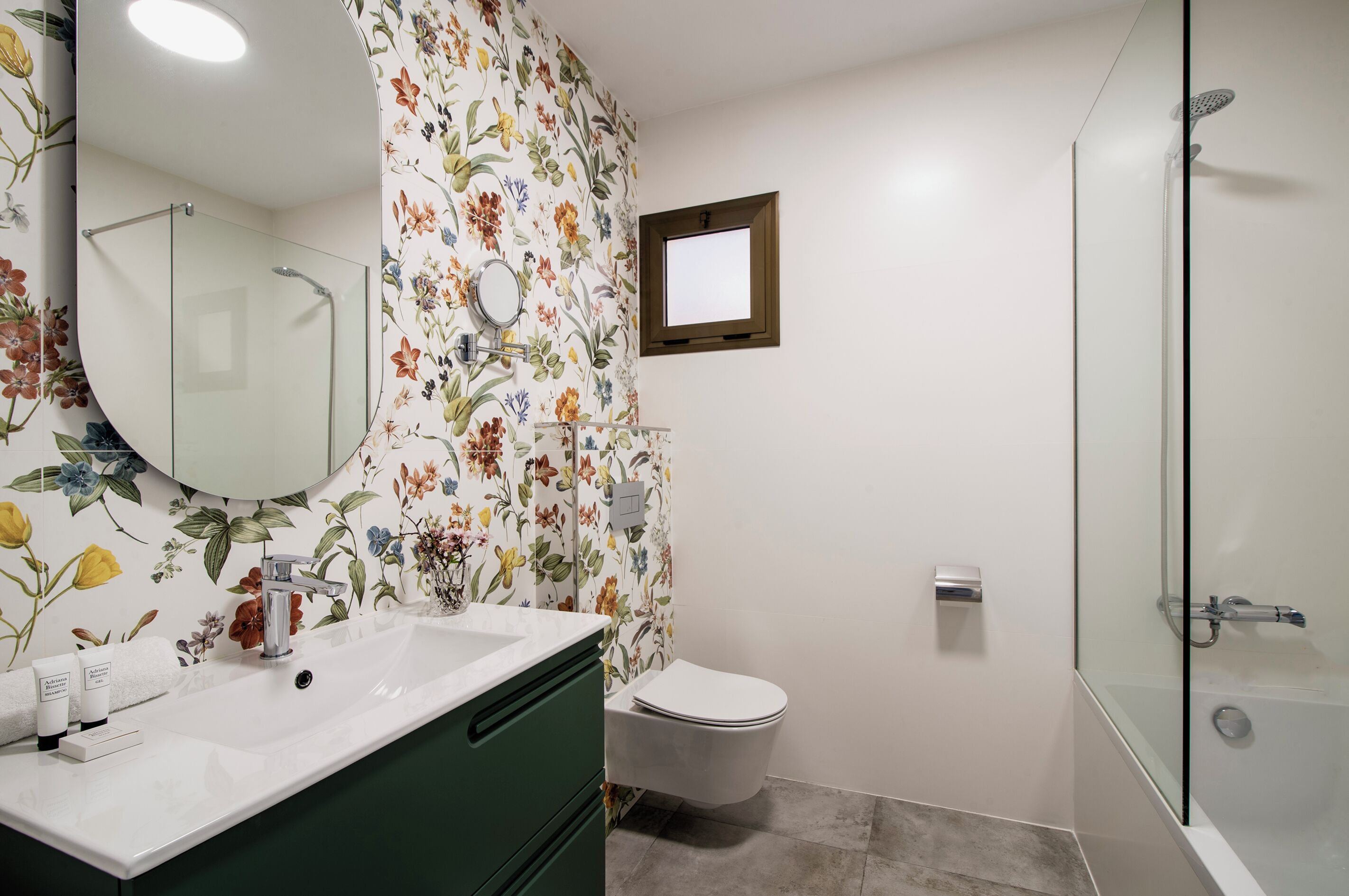 A bathroom with a floral wallpaper, a white sink, a toilet, and a glass-enclosed shower.