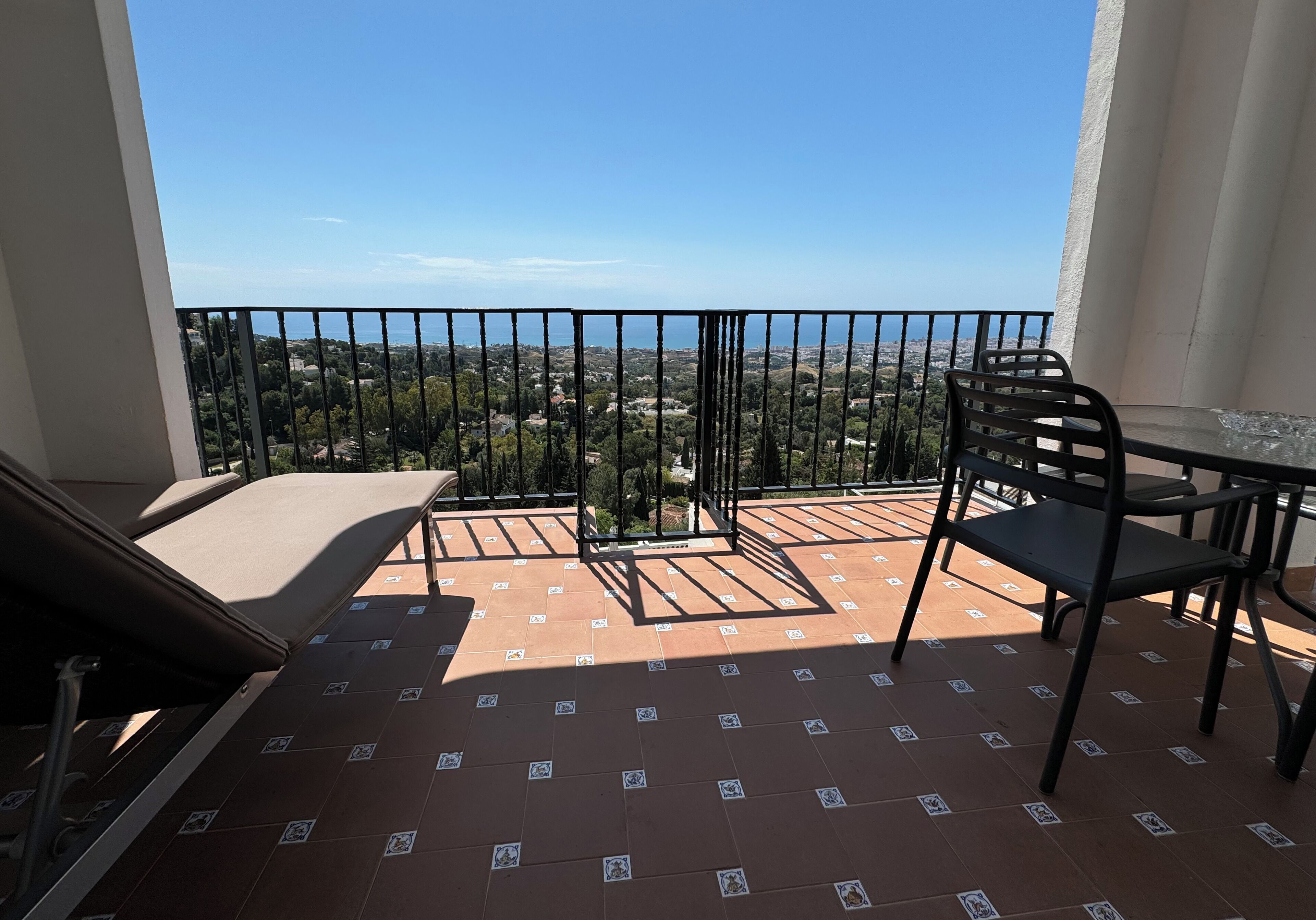 A balcony with a view of a cityscape, a table, and two chairs.