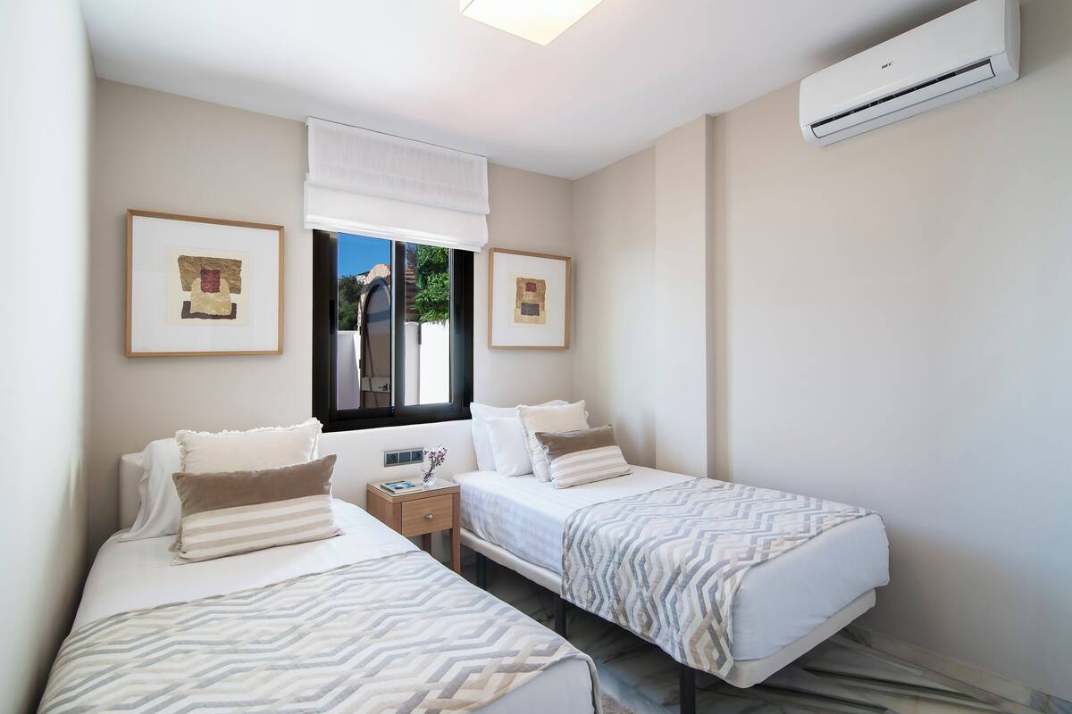 A bedroom with two beds, a window, and an air conditioning unit.