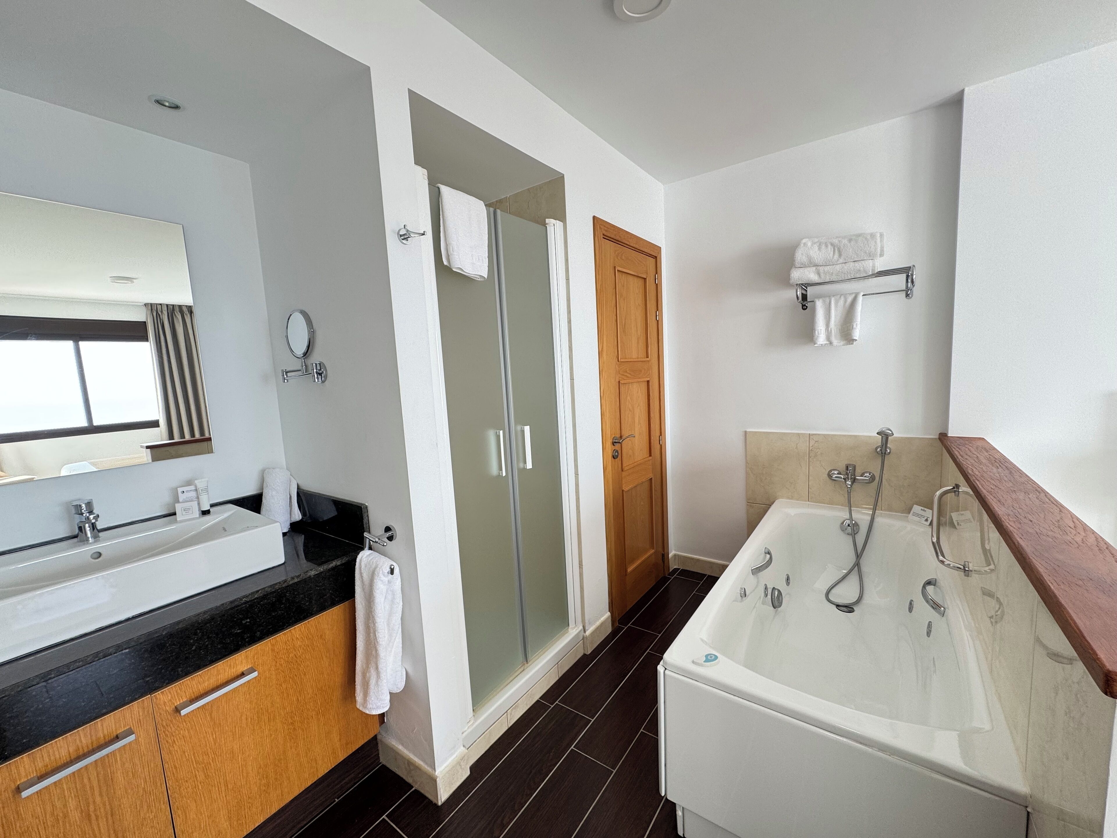 A modern bathroom with a large mirror, a double sink, a shower enclosure, and a bathtub.